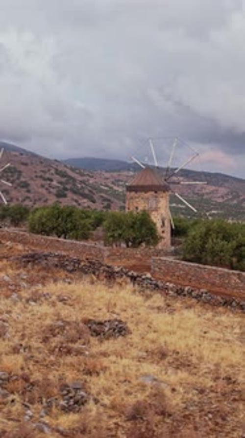 Des moulins à vent s'élèvent au-dessus de collines arides dans un paysage isolé et nuageux