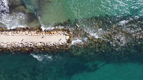 Old ruined pier on pebbly beach with transparent water. Aerial top down view of breakwater.