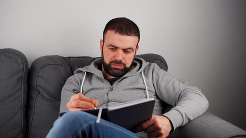 Man Writing On Notebook While Sitting On The Sofa. - close up shot