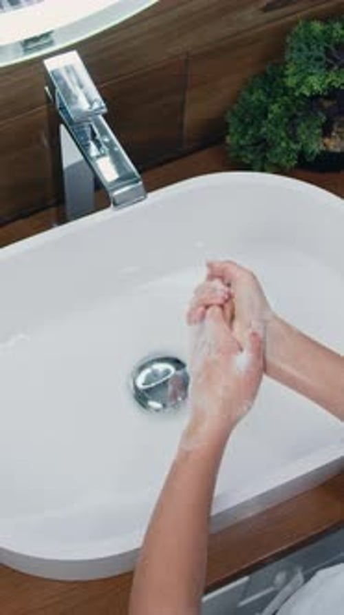 Cute Little Girl Washing Her Hands with a Hand Wash Gel in Sink Rinsing with Hot Water Over Bathroom