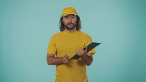 Un repartidor con uniforme amarillo que escribe en un papel entrega los documentos de pedido para que los firme ante la cámara