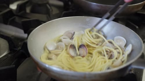Cuisiner des pâtes spaghettis avec des palourdes dans la poêle d'un restaurant