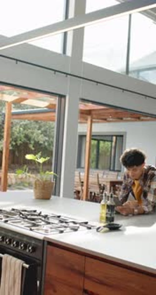 Vertical video: Young person using tablet and drinking coffee in modern kitchen at home