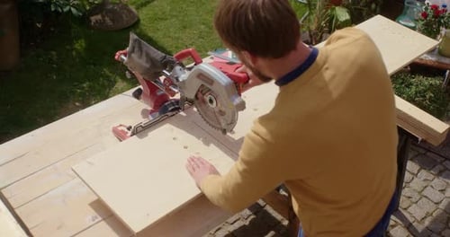 Man Cutting Wood with Power Saw Outdoors