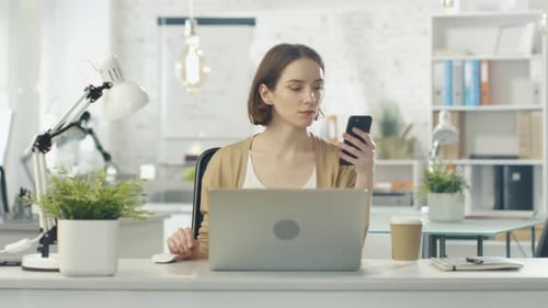Woman Using Laptop and Smartphone in Modern Office