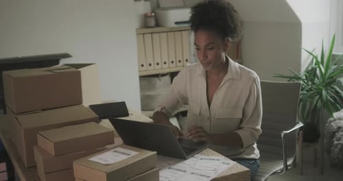 Young Woman Using Laptop at Desk with Boxes