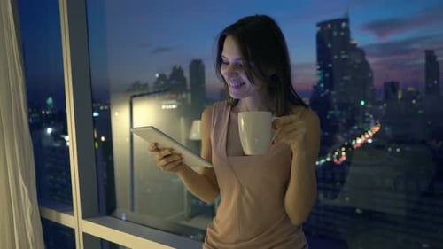 Woman Using Tablet and Drinking Coffee at Night