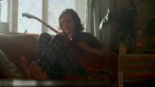 Man plays electric guitar while sitting on sofa