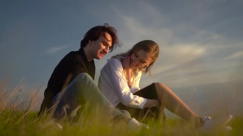Romantic Couple Sitting in a Grassy Field at Sunset