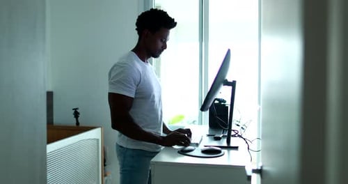 Schwarzer Mann steht vor einem Computerbildschirm und arbeitet von zu Hause aus