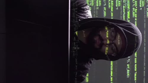 Männlicher Hacker oder Programmierer, der an einem Computer arbeitet. Dunkler Hintergrund mit grünen Codezeilen. Vertikaler Schuh
