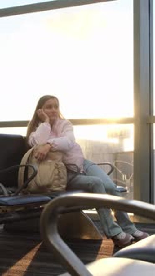 Calm Female Traveler Waiting in an Airport Departure Lounge While Using a Smartphone By a Window at