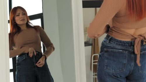 Woman Trying to Button Tight Jeans in Mirror