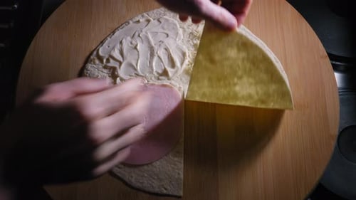 A close up shot of the hands of a chef carefully folding a round flour tortilla wrap into quarters a