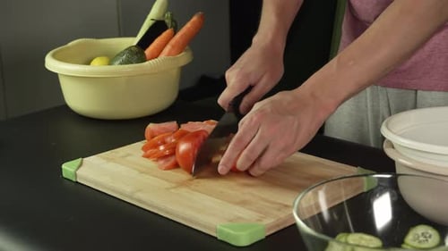 Hands of middle man european slices a tomato with kitchen knife on cutting board, right side view