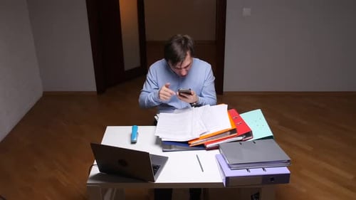 Stressed Office Worker Throwing Phone at Work with Folders and Laptop