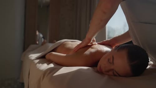 Friedliche Spa-Wellness-Sitzung mit einem Therapeuten, der die Frau auf dem Massageliegen in Soft Natural zurückmassiert