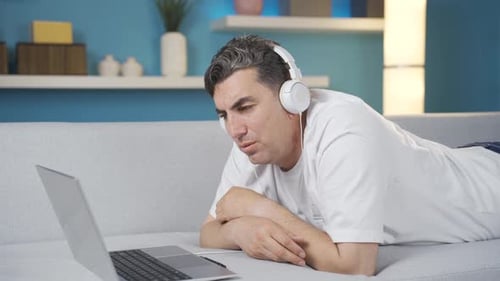 Man Using Laptop With Headphones On Couch
