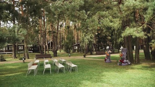 View of Wedding Floral Decorated Arch and White Chairs Under the Pine Tree Slow Motion Outside