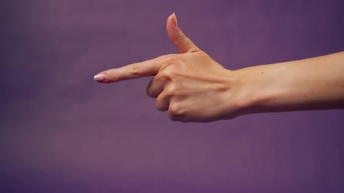 Hand Making Gun Shape Against Purple Background