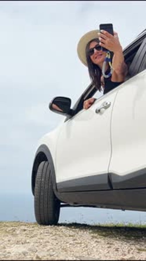 Frau macht Selfie mit dem Auto auf dem Aussichtspunkt Meereslandschaft (vertikal)