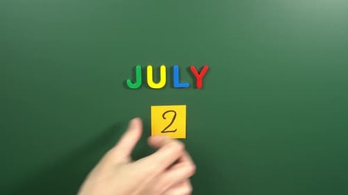Hand sticking a sticker 2 July calendar day on school board. 2 date of July. Second day July