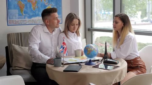 A Female Travel Agent Tells a Young Couple About a Trip in a Travel Agency