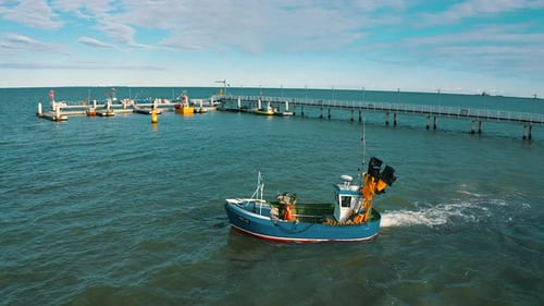 Aerial view of fishing boat on the sea with pier in the background
