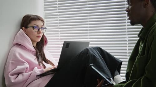 Des programmeurs multiethniques réfléchissent à un projet assis sur le rebord de la fenêtre