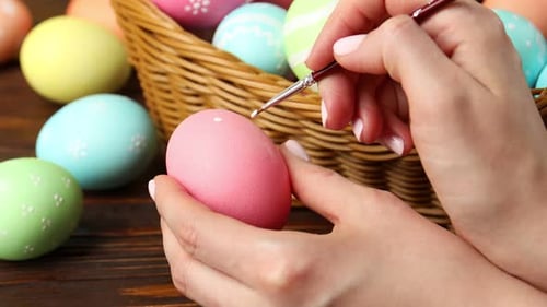 Woman painting Easter egg at wooden table, closeup
