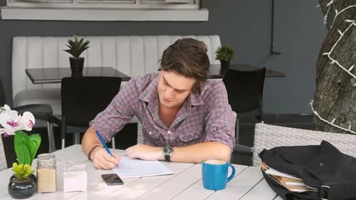 Man Writing at Outdoor Cafe Table