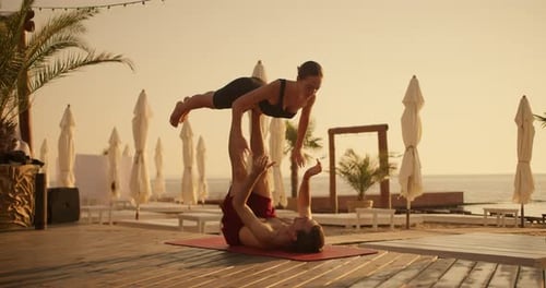 The Guy Holds the Girl Up with His Legs the Couple Does Yoga Combined with Acrobatics on a Red