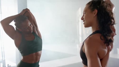 Stretching and chatting, two women in gym wearing athletic wear, staying fit