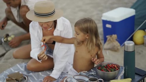 Mother and Daughter Enjoy a Healthy Picnic on a Sandy Beach Sharing Fresh Salad and Snacks Under the