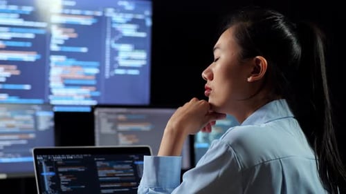 Vista trasera de una programadora asiática pensando mientras escribe código con una computadora portátil