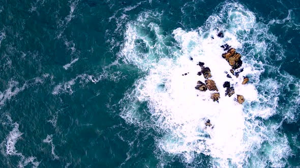 Abstract top down aerial riser over sea rocks as waves crash creating ...