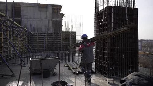 Construction Worker Carries Plank on Building Site