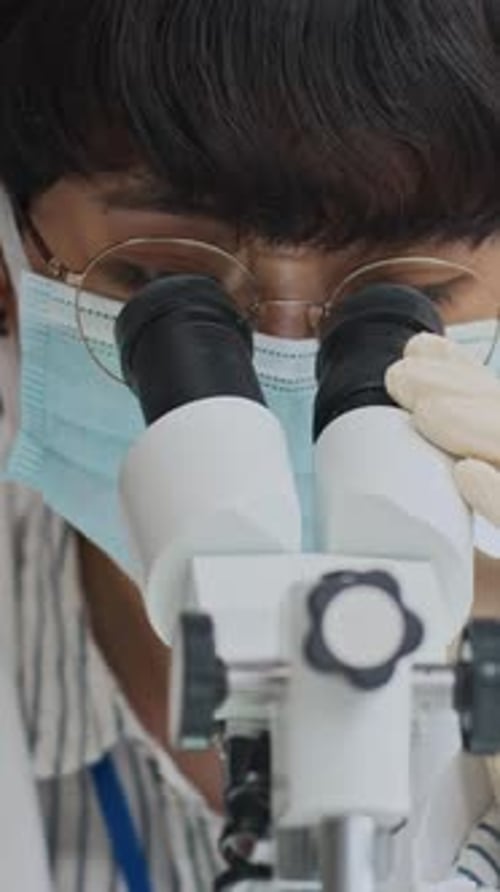 Wissenschaftlerin mit Brille schaut durchs Mikroskop