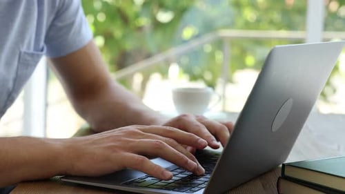 Mann arbeitet drinnen am Laptop am Holztisch, Nahaufnahme