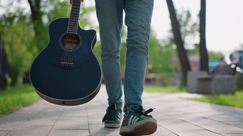 Musician Strolling Outdoors Musician Casually Traverses Sunlit Urban Park Pathway Casual Guitarist