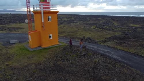 Drone pullback from the orange lighthouse revealing the tourists waling and the vast Atlantic Ocean