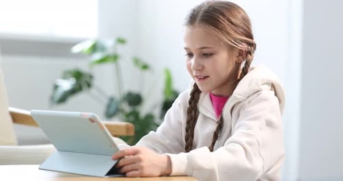 Little girl using modern tablet at wooden table indoors