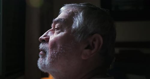 Close-up profile of elderly man gazing up while sitting indoors, peaceful and reflective moment