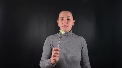 Woman Tasting Food on Fork Against Dark Background