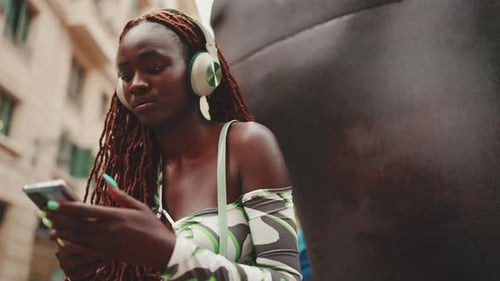 Gorgeous woman sits with headphones outside on the street and uses mobile phone