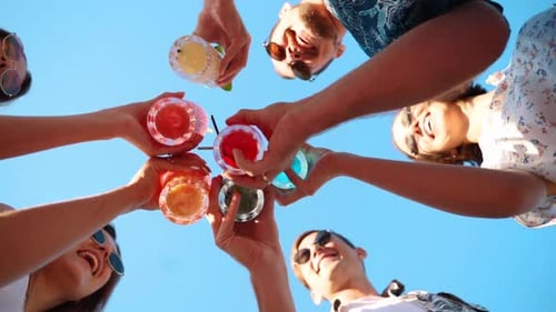 Vue à angle réduit d'amis s'amusant lors d'une fête à la piscine avec des verres à tinter avec des cocktails d'été colorés