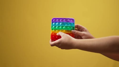 Female Caucasian Hand Playing Multicolored Fidget Toy in Slow Motion at Yellow Background