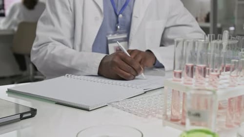 Unrecognizable Black Scientist Writing at Desk, Surrounded by Test Tubes in Lab