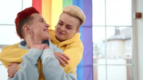 Smiling Couple Embraces Near Rainbow Flag Indoors