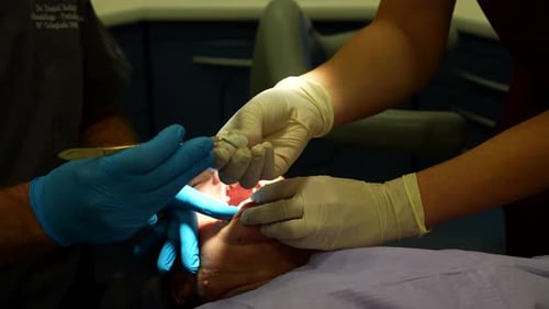 Dentist removing stitch from patient’s mouth with assistant cleaning tools
